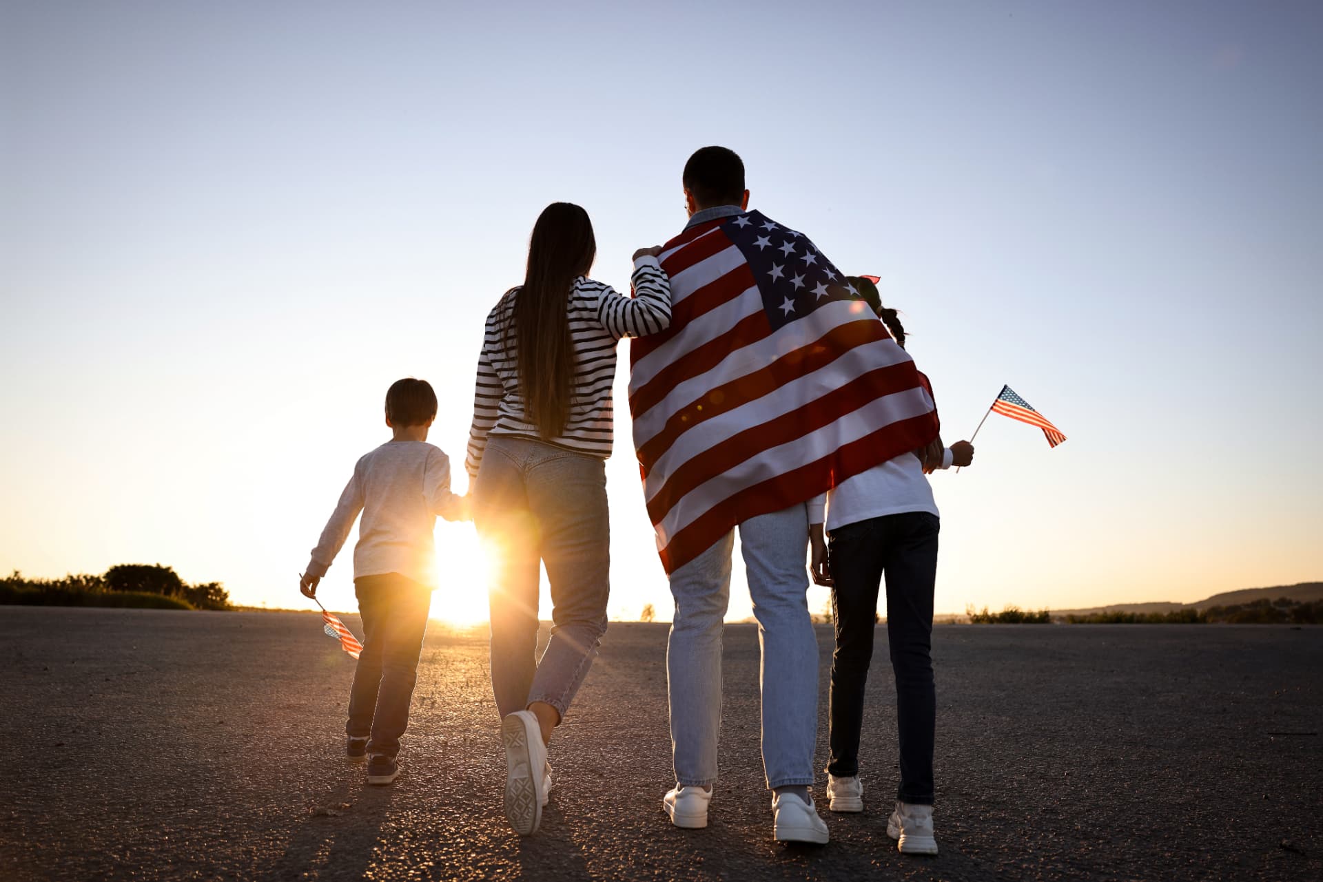 A family walking together outdoors wrapped in an American flag at sunset